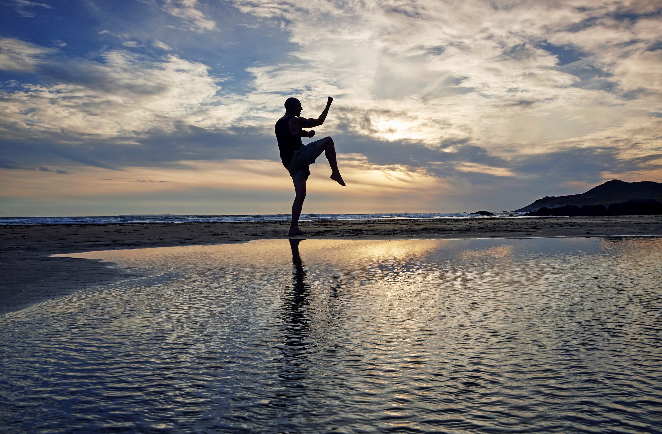 Silhouette of man practicing kung fu moves on beach at sunset.